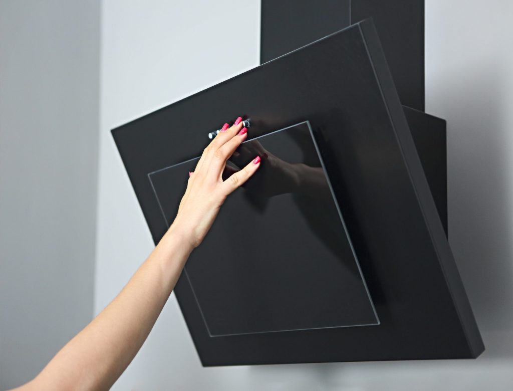 A hand reaching to the glass panel of an angled black range hood
