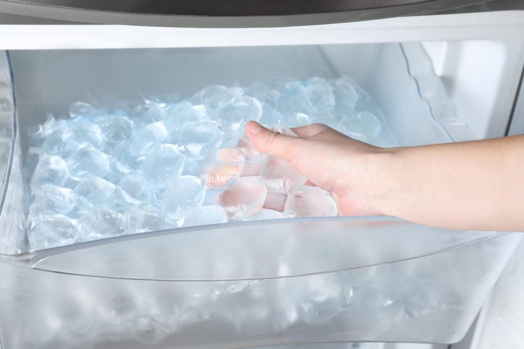 A hand reaching into a freezer bin heaped with ice cubes