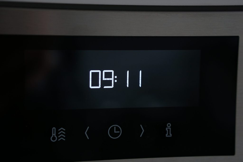 The dark touch panel of a wall oven showing the time and its symbols
