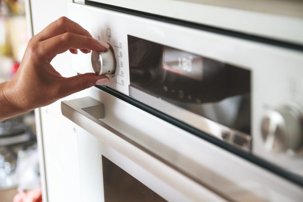 A hand on the control dial of a wall oven whose display reads 180