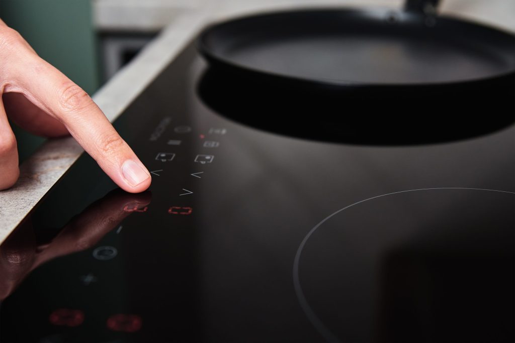 A finger on the lit touch control strip of a black cooktop