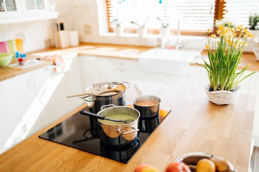 Two pans simmering on a black induction cooktop set into a wooden island