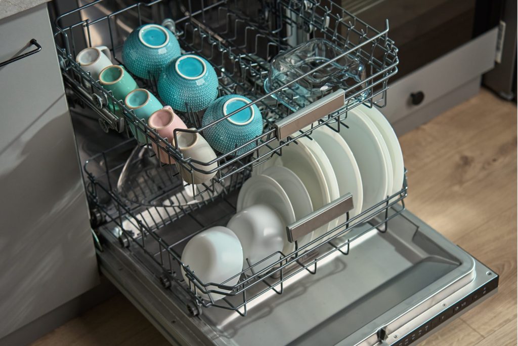 An open dishwasher loaded with clean crockery and mugs, standing open in a home kitchen