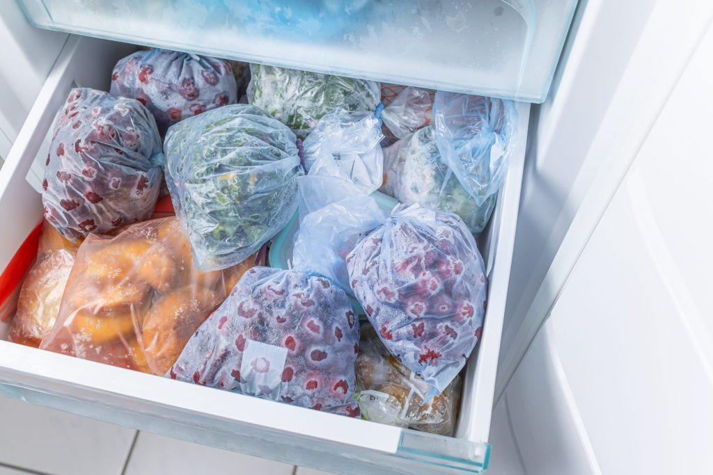 An open freezer drawer packed with bagged frozen fruit and vegetables