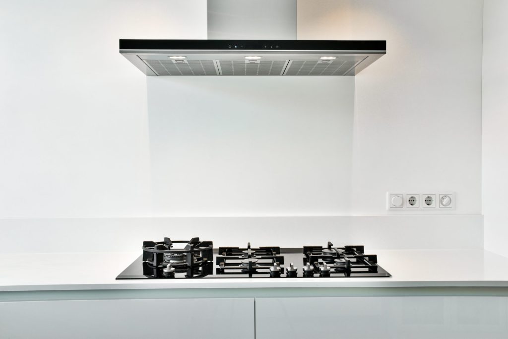 A wall-mounted stainless range hood above a black gas cooktop in a white kitchen