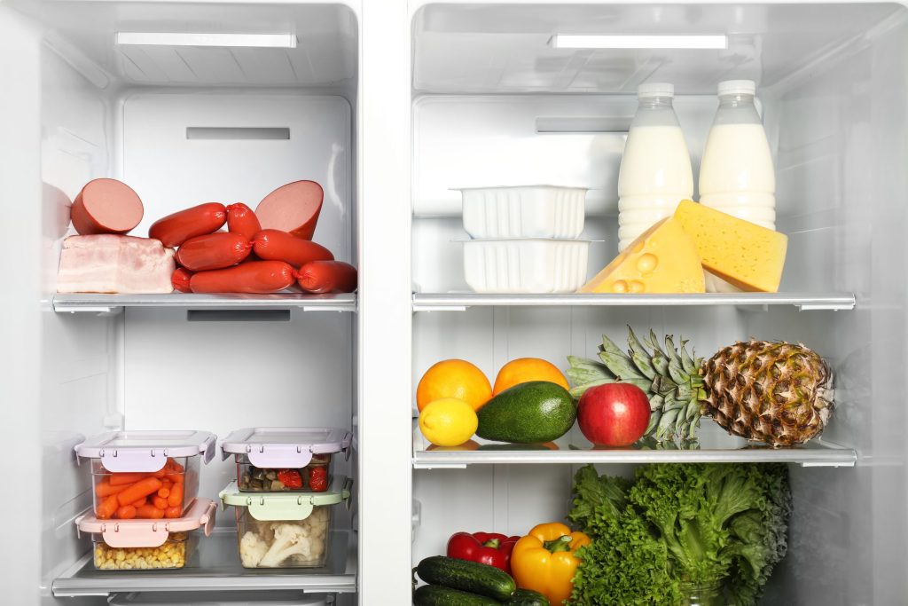 A refrigerator standing open, both sides stocked with produce, dairy and cold cuts